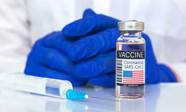 Vaccine vials with USA flags on it, close up photo of American covid-19 vaccine, vaccination concept background with doctor hands in blue gloves
