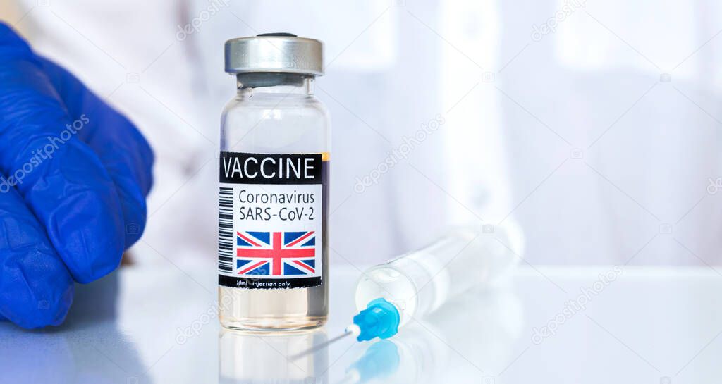 United Kingdom flag on the vaccine vial, coronavirus covid-19 vaccination concept banner with doctor hand in blue gloves and medical suringe, copy space photo