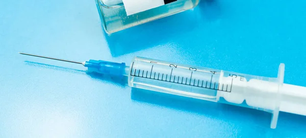 Vaccination banner with medical syringe close up on a blue background, glass table in hospital