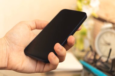 Adam ev içi arka planda siyah akıllı telefonu tutuyor, cep telefonu kullanma kavramı