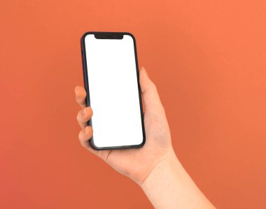 Kharkov, Ukrayna - 5 Mayıs 2021: Ellerinde boş beyaz ekran, turuncu arkaplan fotoğrafı olan Apple iPhone 12
