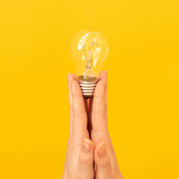 Concept of the new idea, light bulb in hand close-up on orange yellow background, isolated 