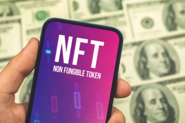 Yenilik teknolojisi ve kripto sanatı ekranda NFT logosu elinde cep telefonu, kriptografik ve kripto para birimi konsepti arka plandaki fotoğrafta dolar.