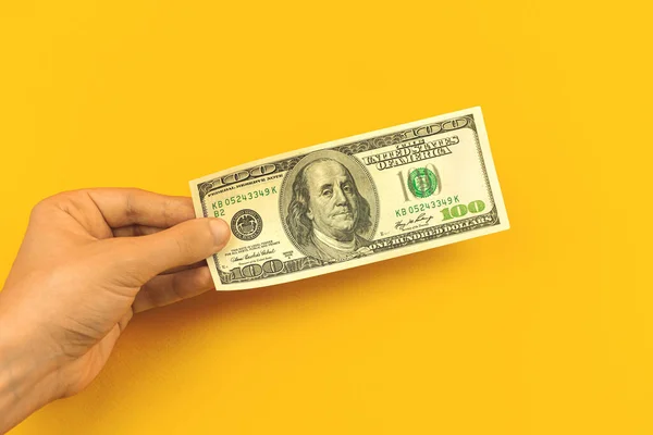 男の手は オフィステーブル 銀行預金の概念の黄色の背景に100ドル札を保持 — ストック写真