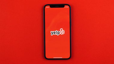 Kharkov, Ukrayna - 28 Mayıs 2021: Apple iPhone 12 ekranındaki Yelp uygulama logosu kırmızı arkaplan, Yelp uygulaması sosyal ağ ve hizmetleri 