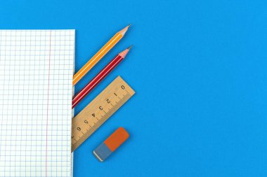 Okul günlerinin ilk konsept kompozisyonu için hazırlan, düz mavi zemin, defter, kalem, tahta cetvel ve silgi ile düz mavi zemin, üst görünüm resmini kopyala