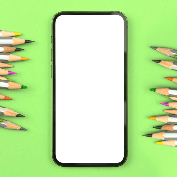 Mobile phone mockup on green school table with colour pencils, copy space, top view