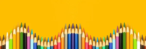 School banner with wavy color pencils border on a yellow table background with copy space, top view