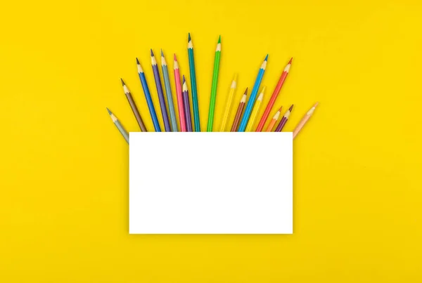 Creative school mockup with blank white paper and color school pencils on desktop, yellow background, copy space and top view