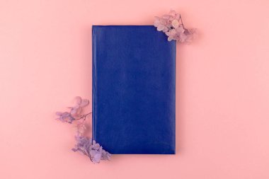 Boş mavi deri defter. Kurumuş çiçek kompozisyonu, pembe arkaplan, üst görünüm. 