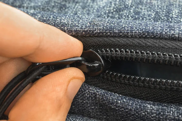 Fingers hold zipper bag on a backpack close-up background