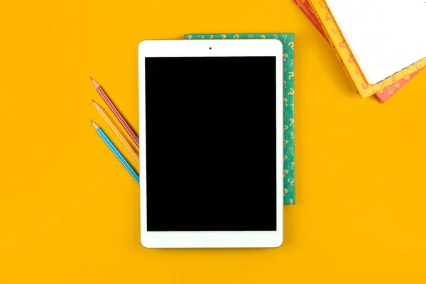 Education concept, students tablet with pencils on the yellow desktop, books with question signs, flat lay and top view