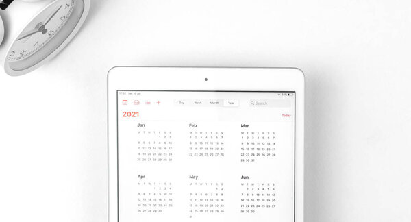 Tablet with open Calendar 2021, white background workspace with alarm clock, business concept 