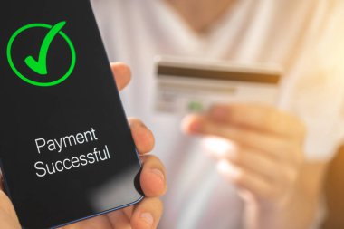 Cep telefonu işlemi, ödeme başarılı ekran ve banka kredi kartı arka planda kadının elinde 