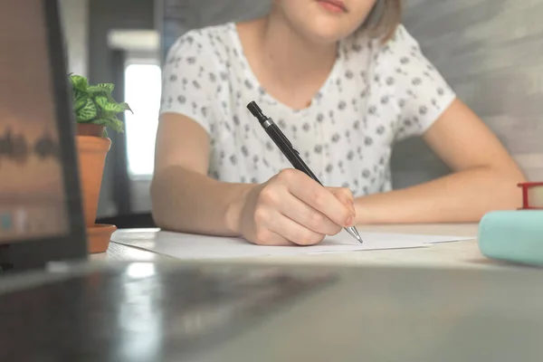 Young student girl holding pencil and writing. Education concept background. Wooden table with laptop and business workspace