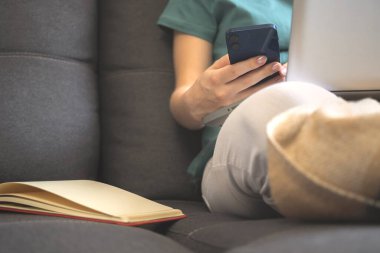 Fosa 'da oturan ve akıllı telefon kullanan kadın. Sonbahar günlerinde kitap ve dizüstü bilgisayarla rahat bir hafta sonu.