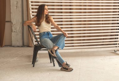 Sıradan moda konsepti, atölyede kot pantolonlu genç bir kadın, sandalye konseptinde poz veriyor. 