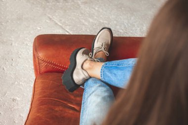 Deri sandalyede kot pantolon ve şehirli züppeleriyle oturan genç kız. Sokak modası ve konsept 