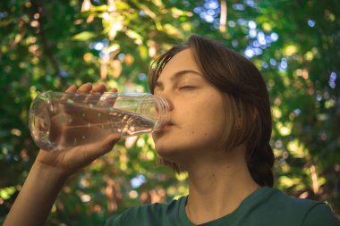 Genç yürüyüşçü kız orman fotoğrafındaki suyu içerken dinleniyor.
