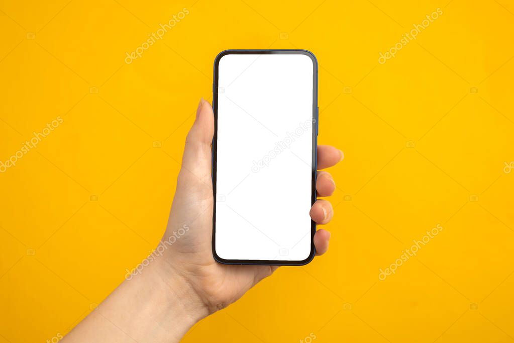 Person holding mobile phone with blank white screen on a yellow background, copy space