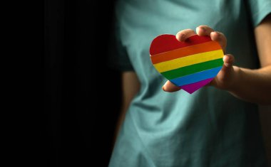 Kopya uzay fotoğraflı LGBT topluluk arkaplanı. Kalp şeklinde LGBT gökkuşağı bayrağı ve sembolü olan bir kız eli. Hoşgörü, lezbiyen ve eşcinsel hakları kavramı