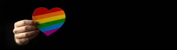 LGBT Pride rainbow heart in hand. Banner with black background and copy space, concept of tolerance