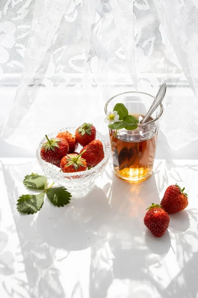 Cup of tea and wild strawberries on a white lace background — Stock Photo, Image