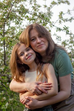 Güzel kızlar çiçek açan elma ağaçlarının arasında yürüyorlar. Anne ve kızı taze doğayla vakit geçiriyorlar. Ruh hali konsepti.