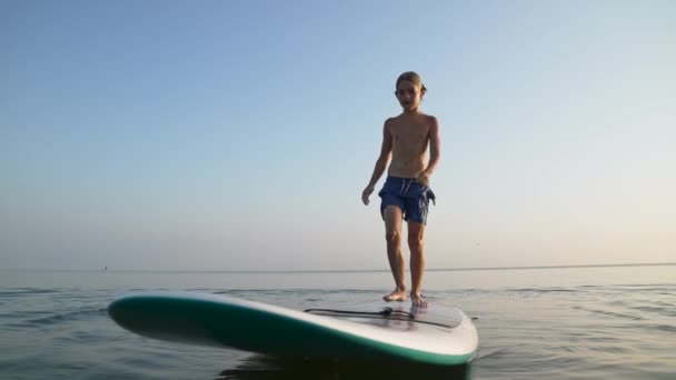 海のビーチで休暇を楽しんで幸せな子供 ボーイ面白いジャンプから水にボード上の旅行休暇で日没 — ストック動画