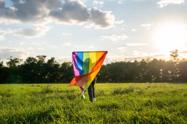 Aşkın sembolü, özgürlük ya da LGBT gurur konsepti. Mavi gökyüzü arka planında gökkuşağı bayrağını tutan kız, yazın açık havada. Özgürlük hakkı, eşitlik ve yasal evlilik gururu.