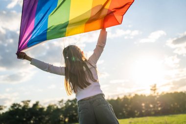 Aşkın sembolü, özgürlük ya da LGBT gurur konsepti. Gökkuşağı bayrağını mavi arka planda tutan kız yazın açık havada. Özgürlük hakkı, eşitlik ve yasal evlilik gururu.