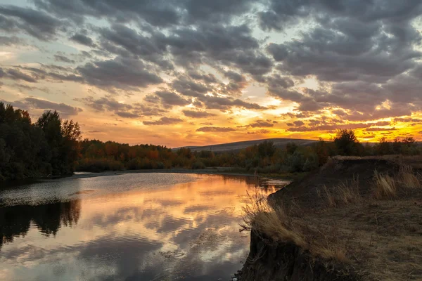 Evening glow of cloudy sky over river valley with sunset reflection in water