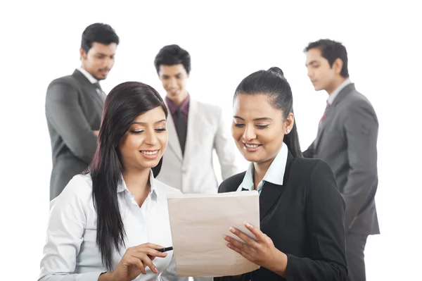 Two businesswomen reading a document with their colleagues in th — Stock Photo, Image