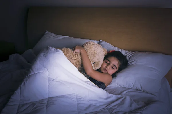 Menina dormindo na cama com um ursinho de pelúcia — Fotografia de Stock