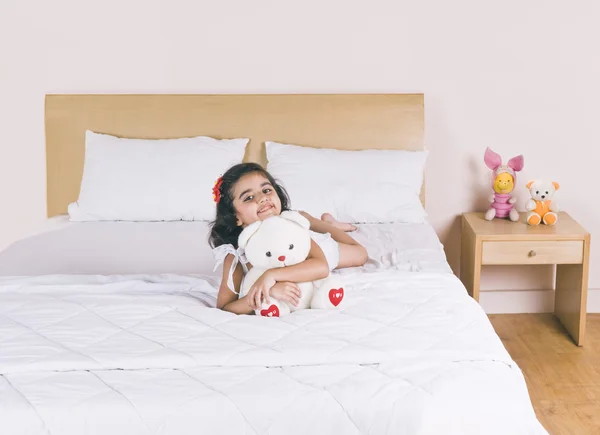 Menina deitada na cama segurando um ursinho de pelúcia e sorrindo — Fotografia de Stock