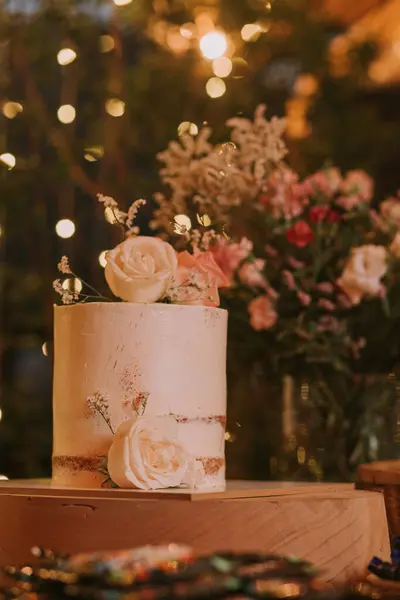Ahşap bir masanın üzerinde pembe çiçeklerle süslenmiş düğün pastası..