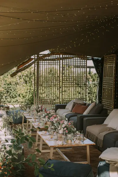 Ahşap masa, gri sandalyeler, çiçekler, bardaklar ve mumlarla sosyal etkinlik çadırı.