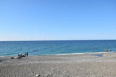 Üzerinde insanların yürüdüğü bir sahil ve bir su kütlesi.