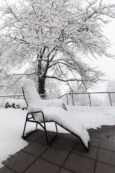 Snow-covered deck chair in a snowy park in cloudy weather in January.