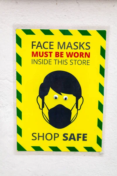 A wall sign stating that face masks must be worn while inside the store. Comedy googly eyes have been stuck on the eyes