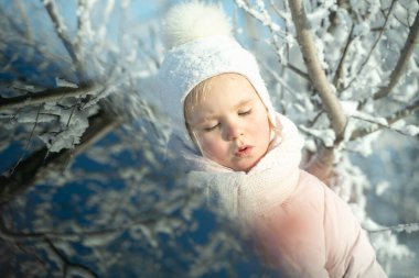 Sıcak beyaz şapkalı ve eşarplı bir çocuk kış ormanlarında yürürken karla oynar, kar yağışı, kış büyüsü, parlak duygu, cildi dondan korur.