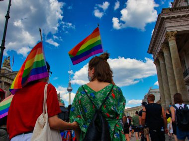 Berlin, Almanya - 26 Haziran 2021 - İki lezbiyen kadın, arka planda Berlin TV kulesi bulunan Christopher Street Day (CSD) gösterisinde gökkuşağı bayrağını havaya kaldırdı