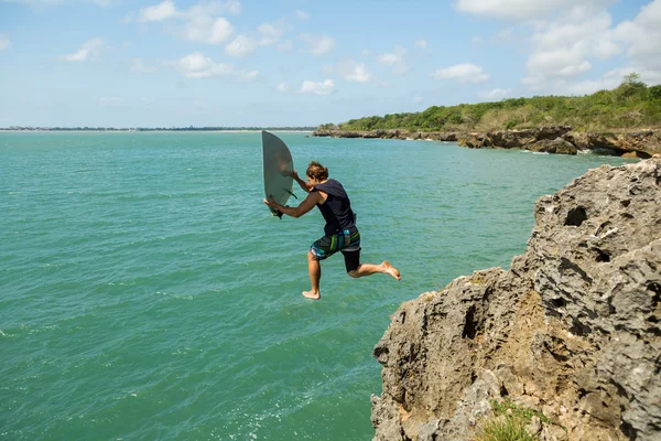 Surfer jumps off a cliff into the ocean. Indonesia Bali