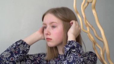 Makyajlı bir elbise giymiş genç bir kız aynaya bakar ve saçlarını düzeltir. Tek başıma. Gri arka planda mavi gözlü genç kız. Modellik. Pozisyon