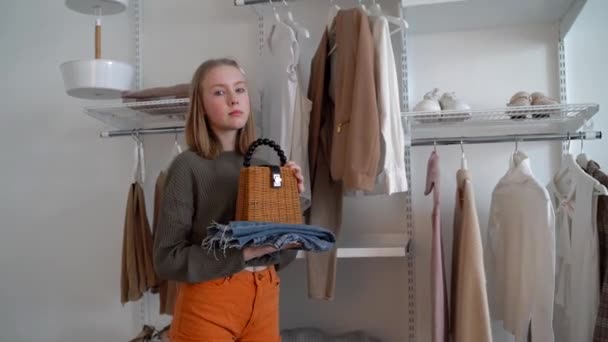 Nastolatek trzyma słomkę i dżinsy i stoi obok garderoby. Moda dla nastolatki. Parsowanie ubrań i porządkowanie rzeczy. — Wideo stockowe