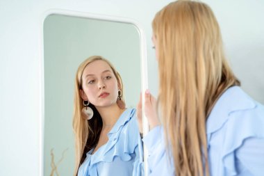 Neşeli sarışın genç bayan mavi bluzunun içindeki yansımasına bak, şenlikli kıyafet.