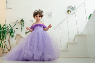 Portatif mutlu esmer kız çocuğu. Mor elbiseli, incili taç takan. Annesinin elini tut.