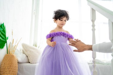 Portatif mutlu esmer kız çocuğu. Güzel mor elbiseli, inci taclı. Babayı elle tutun.