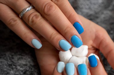 Güzel manikürlü insan parmakları mavi renkli siyah kot pantolonlu beyaz marshmelow tutuyorlar.