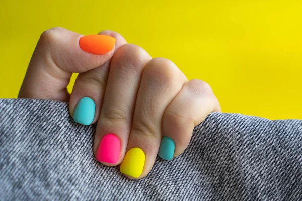 De palm met felgekleurde nagels met oranje, roze, blauw, gele kleuren houden zwarte jeans vast — Stockfoto